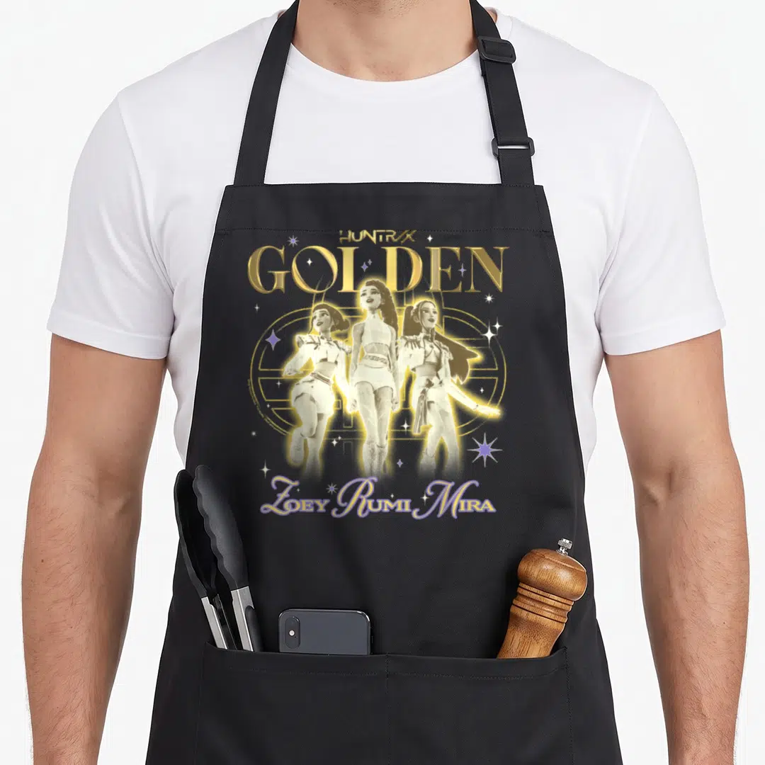 Huntrix golden apron - Three women inside gold circle with text GOLDEN and Zoey Rumi Mira in purple — shown on a black cotton canvas apron against a white background
