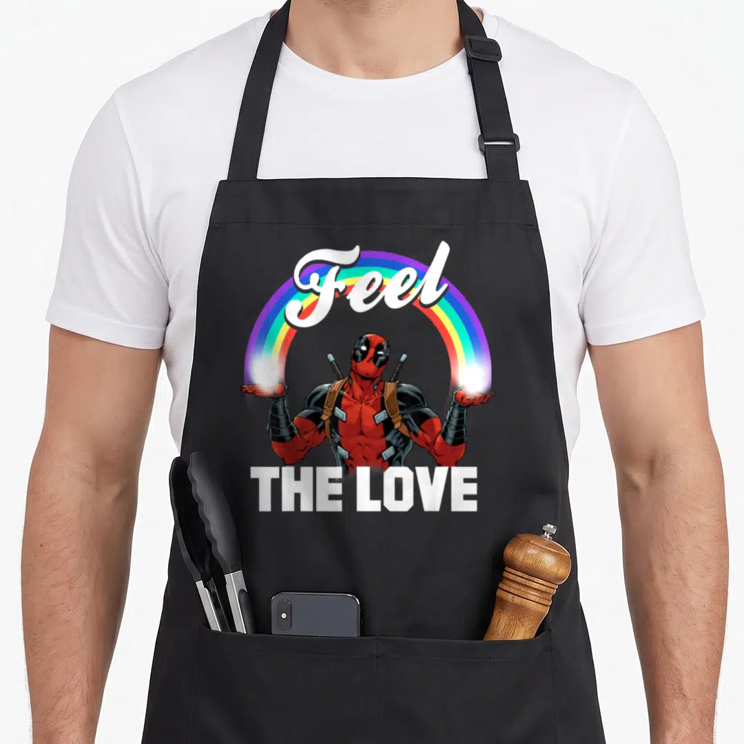 Feel rainbow apron - Deadpool character under arched Feel text and rainbow frame with THE LOVE below — shown on a black cotton canvas apron against a white background