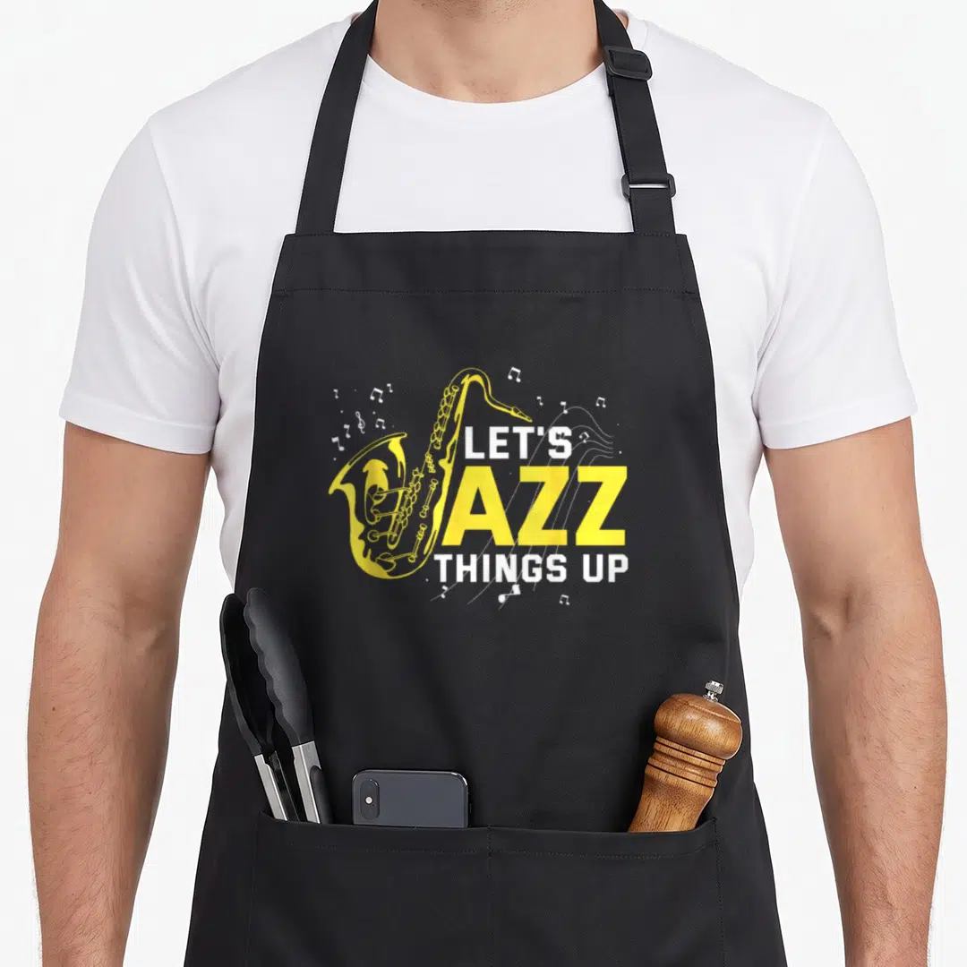 Saxophonist big band apron - Yellow cartoon saxophone overlapping white and yellow text Let's Jazz Things Up — shown on a black cotton canvas apron against a white background