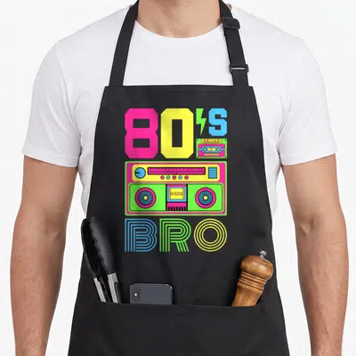 Theme 80s apron - Cartoon boombox with 80S BRO text in pink yellow blue and green — shown on a black cotton canvas apron against a white background