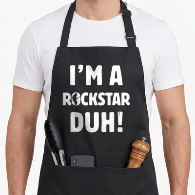 Rockstar easy apron - White stacked text I'M A ROCKSTAR DUH! with guitar silhouette in the letter O — shown on a black cotton canvas apron against a white background