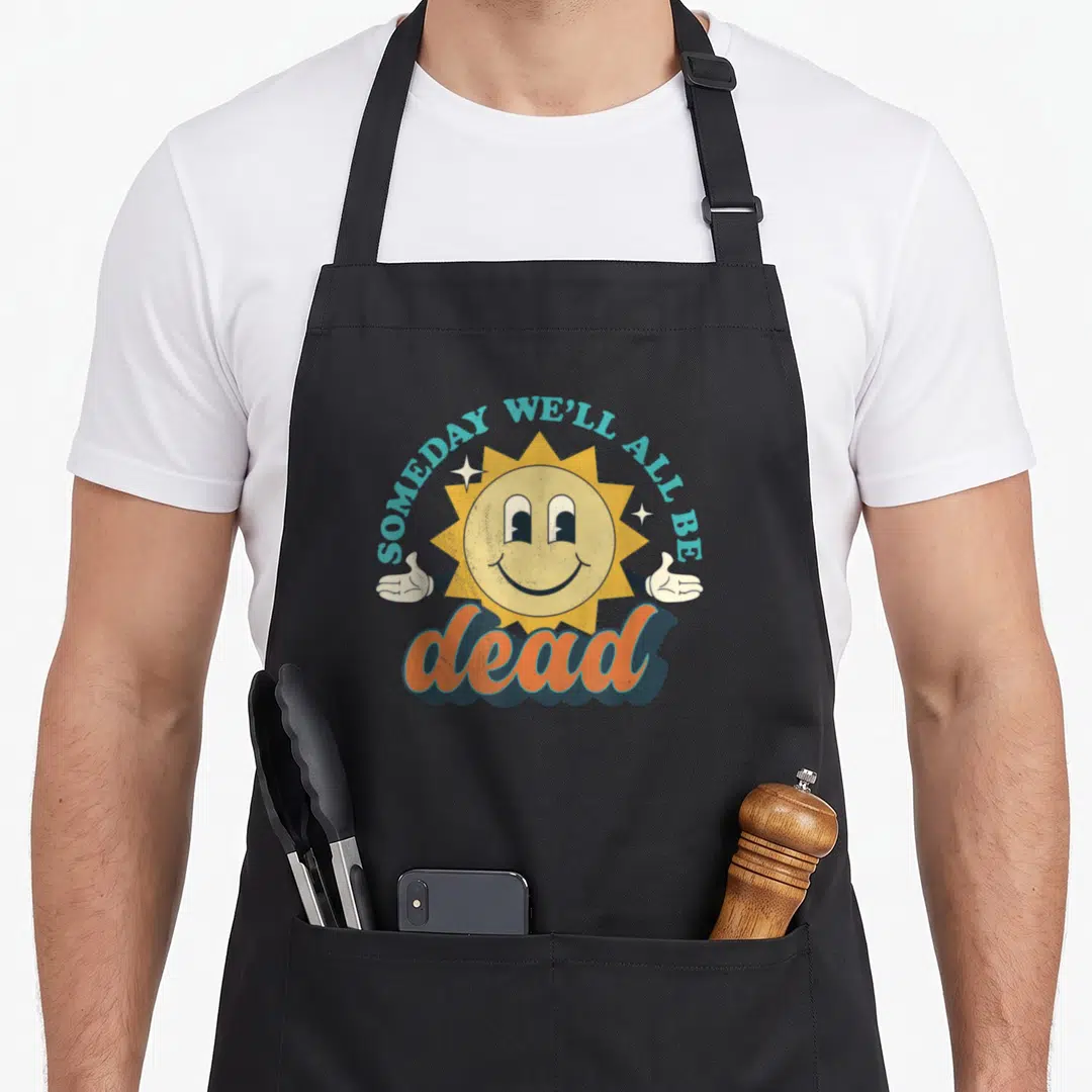 Someday dark humor apron - Smiling cartoon sun with thumbs up and text SOMEDAY WE'LL ALL BE dead in retro colors — shown on a black cotton canvas apron against a white background