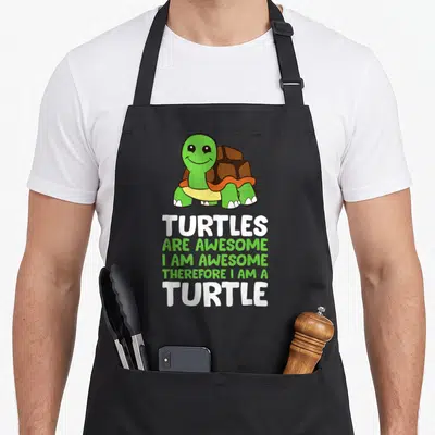 Turtle therefore apron - Cartoon turtle above stacked text TURTLES ARE AWESOME I AM AWESOME THEREFORE I AM A TURTLE — shown on a black cotton canvas apron against a white background