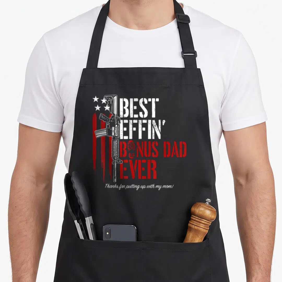 Effin daddy apron - Rifle and stacked text BEST EFFIN BONUS DAD EVER with distressed flag and script footer — shown on a black cotton canvas apron against a white background