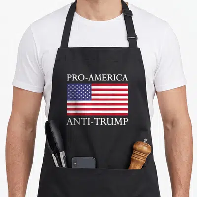 Anti pro apron - PRO-AMERICA and ANTI-TRUMP text surrounding a centered red white and blue USA flag — shown on a black cotton canvas apron against a white background