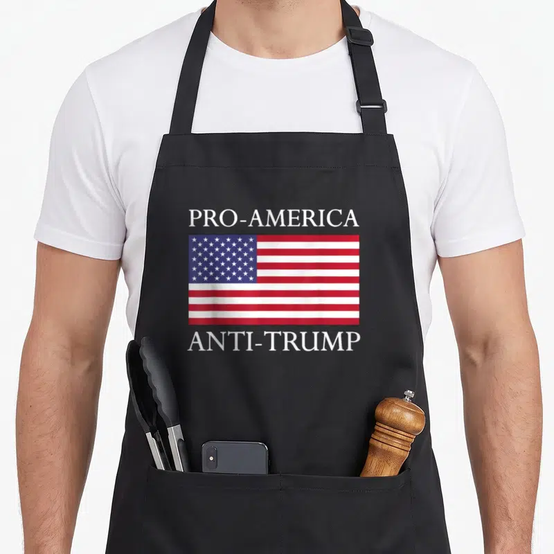 Anti pro apron - PRO-AMERICA and ANTI-TRUMP text surrounding a centered red white and blue USA flag — shown on a black cotton canvas apron against a white background