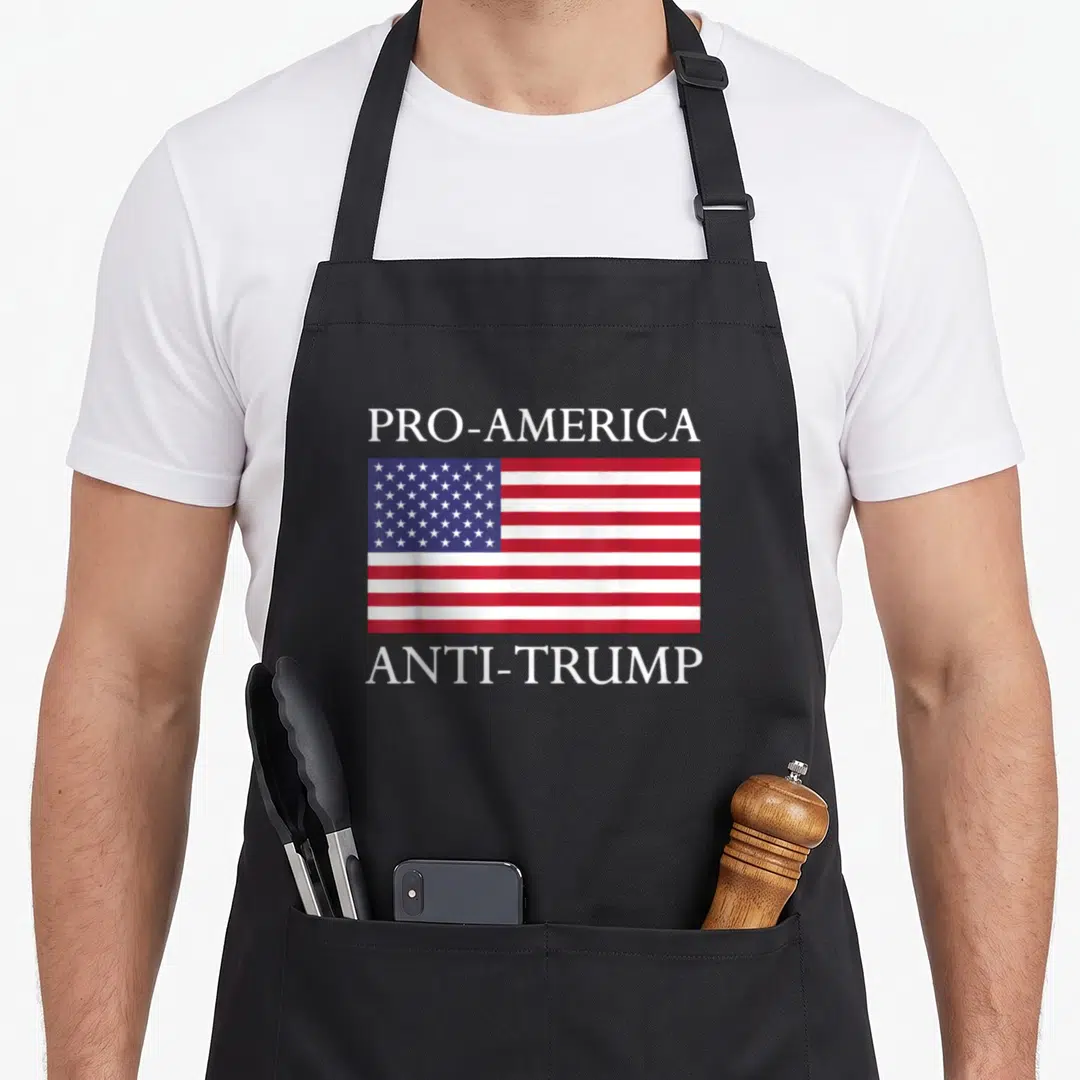 Anti pro apron - PRO-AMERICA and ANTI-TRUMP text surrounding a centered red white and blue USA flag — shown on a black cotton canvas apron against a white background