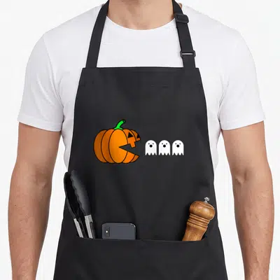 Eating halloween apron - Orange pumpkin with green stem facing three white ghosts in cartoon style — shown on a black cotton canvas apron against a white background