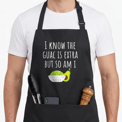 Guacamole mexican apron - White text above green guacamole bowl and halved avocado — shown on a black cotton canvas apron against a white background