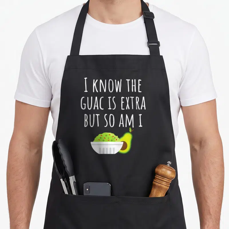 Guacamole mexican apron - White text above green guacamole bowl and halved avocado — shown on a black cotton canvas apron against a white background