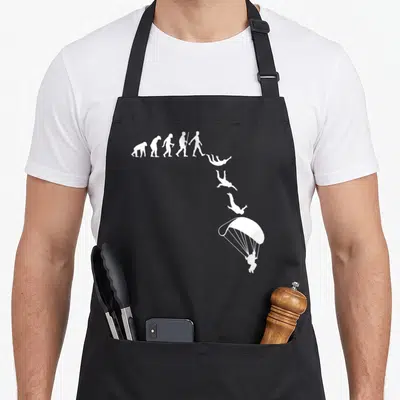 Skydive paragliding apron - White evolution silhouettes curving into a falling parachutist on black fabric — shown on a black cotton canvas apron against a white background