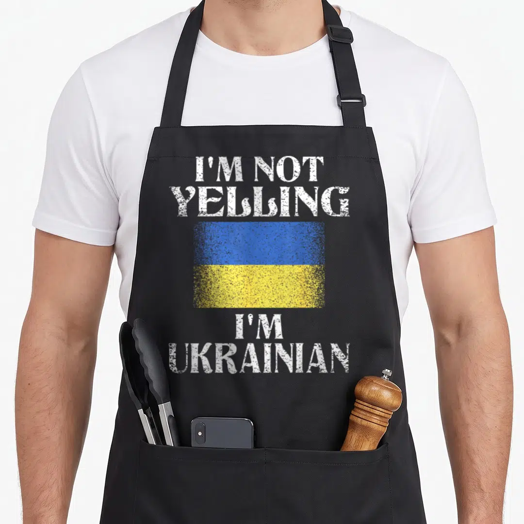 Yelling ukrainian aprons - Distressed white text I'm Not Yelling I'm Ukrainian around a blue and yellow flag — shown on a black cotton canvas apron against a white background
