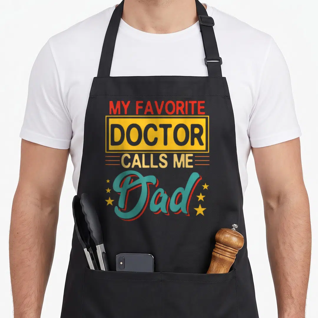 Costume doctor with apron - Stacked vintage text MY FAVORITE DOCTOR CALLS ME Dad with stars in red yellow teal and grey — shown on a black cotton canvas apron against a white background