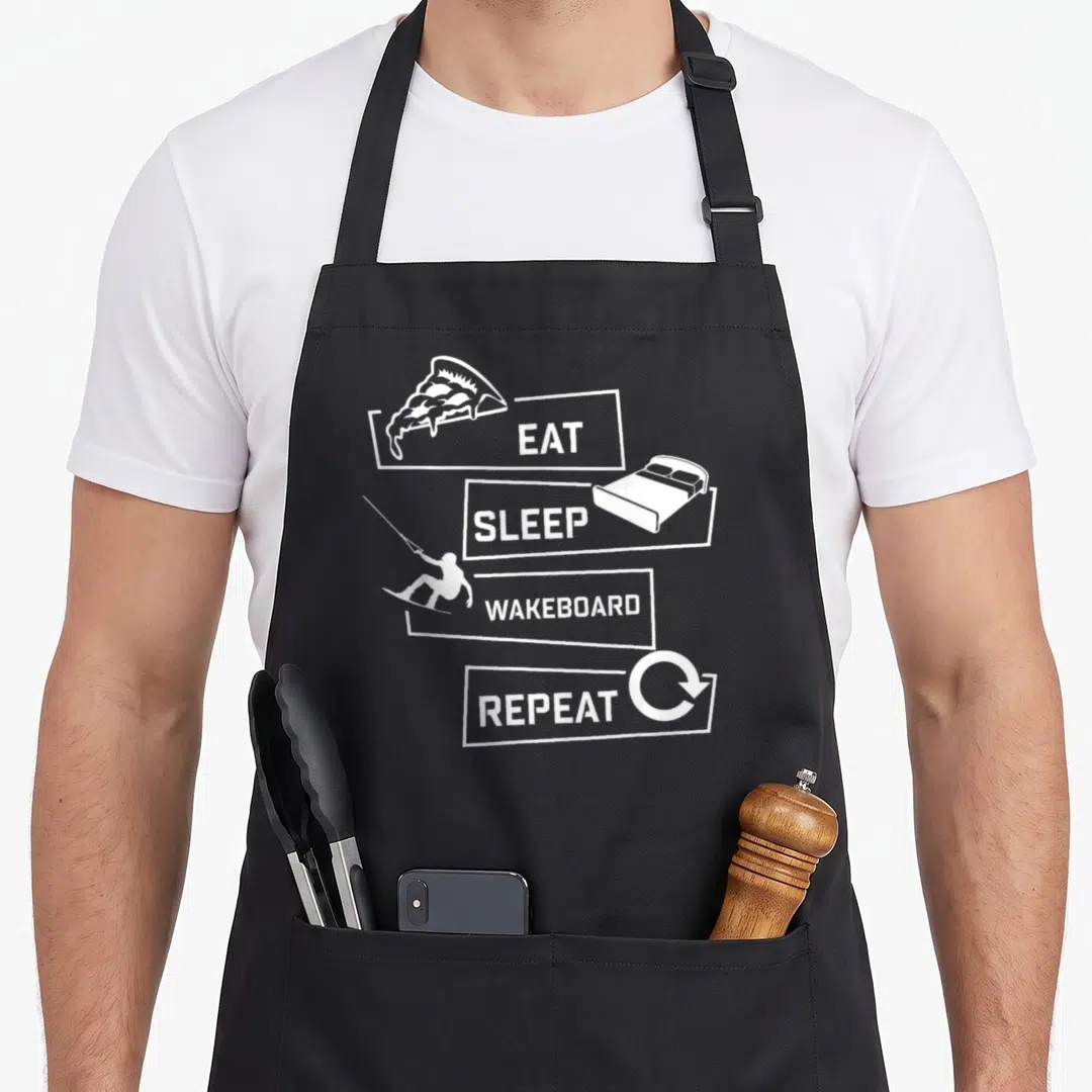 Eat wakeboarding apron - Four white boxes with EAT SLEEP WAKEBOARD REPEAT text and icons of pizza, bed, rider, and arrow — shown on a black cotton canvas apron against a white background