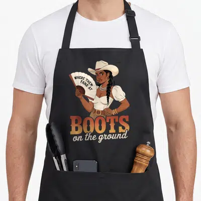 Boot line apron - Woman holding fan reading where them fans at above boots on the ground text — shown on a black cotton canvas apron against a white background