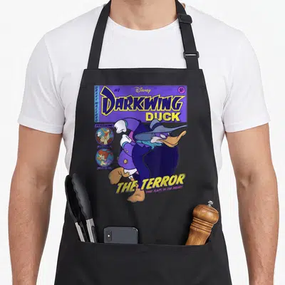 Darkwing duck apron - Vintage comic cover print of Darkwing Duck with Drake Mallard text and supporting character — shown on a black cotton canvas apron against a white background