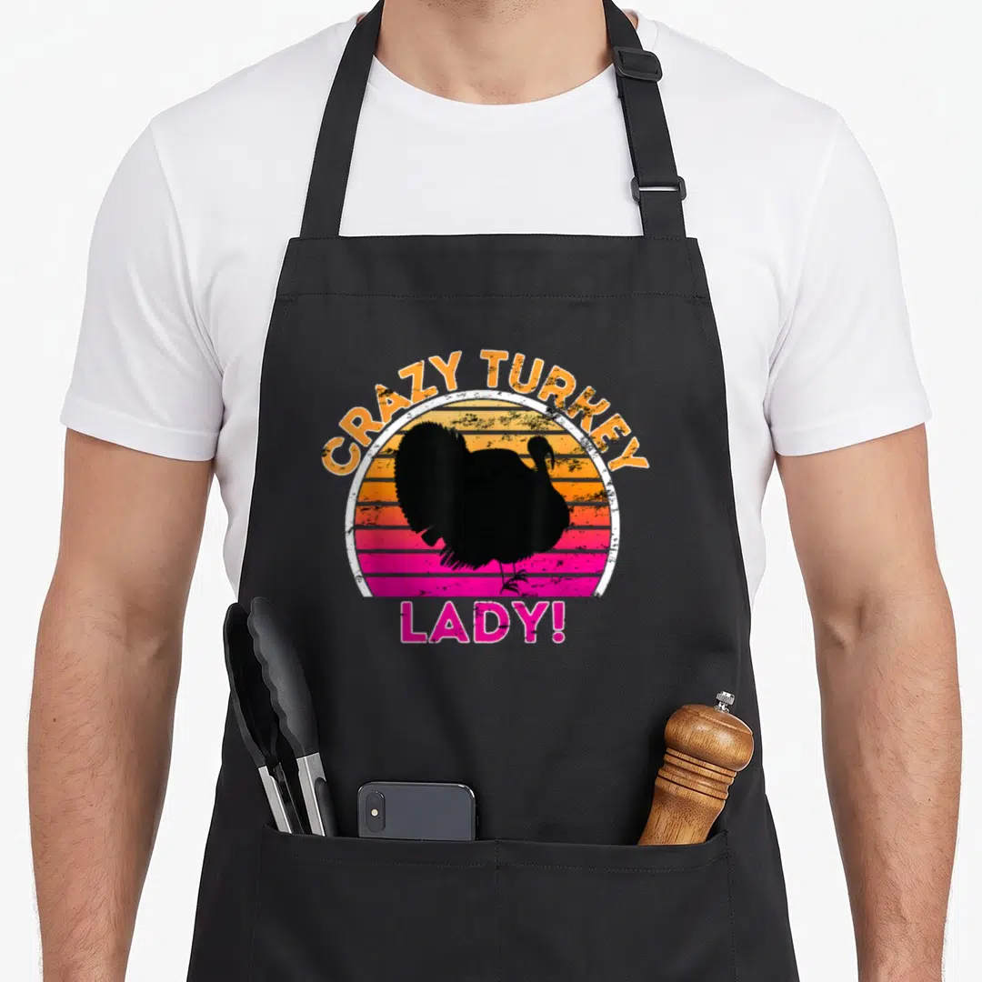 Cool turkey apron - Black turkey silhouette over orange and pink retro sunset stripes with CRAZY TURKEY LADY text — shown on a black cotton canvas apron against a white background