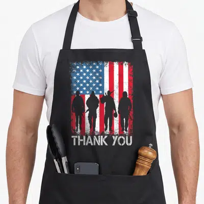 Thank patriotic aprons - Four grey soldier silhouettes on distressed US flag with THANK YOU text — shown on a black cotton canvas apron against a white background