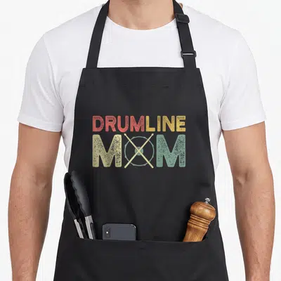 Drumline mother's apron - Distressed DRUMLINE MOM text with drum and crossed sticks in red yellow beige green — shown on a black cotton canvas apron against a white background