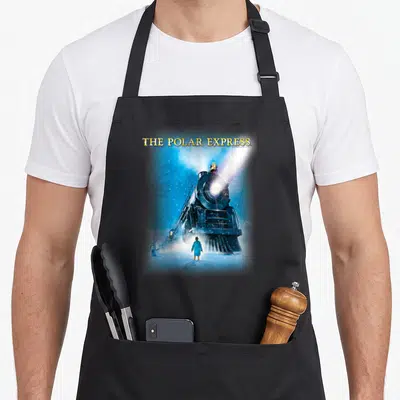 Express polar apron - THE POLAR EXPRESS text above steam locomotive facing forward with boy standing in snow — shown on a black cotton canvas apron against a white background