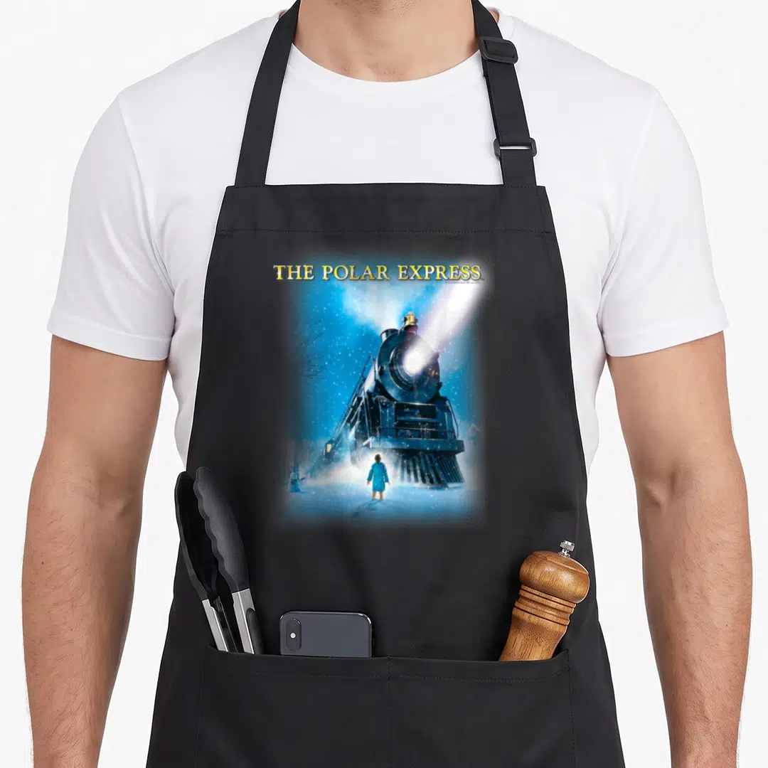 Express polar apron - THE POLAR EXPRESS text above steam locomotive facing forward with boy standing in snow — shown on a black cotton canvas apron against a white background