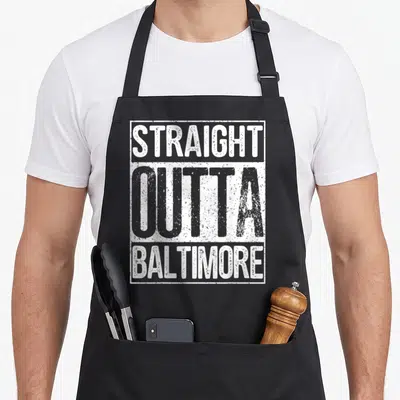 Straight baltimore apron - White distressed text reading STRAIGHT OUTTA BALTIMORE stacked vertically inside — shown on a black cotton canvas apron against a white background