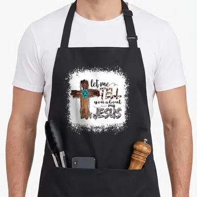 Jesus bible christian apron - Brown cross with turquoise stones and rope next to stacked text on white splatter — shown on a black cotton canvas apron against a white background