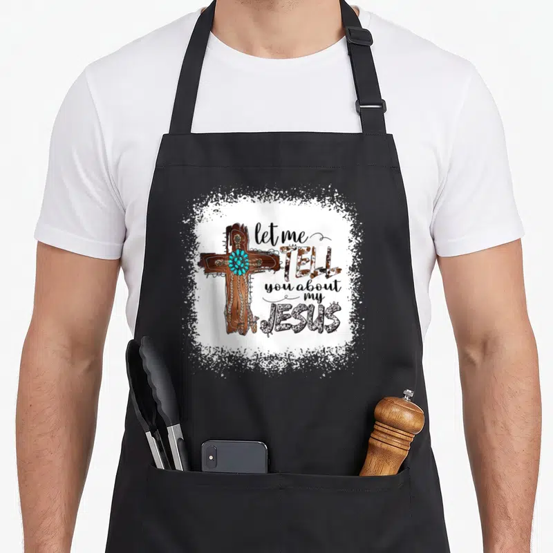 Jesus bible christian apron - Brown cross with turquoise stones and rope next to stacked text on white splatter — shown on a black cotton canvas apron against a white background
