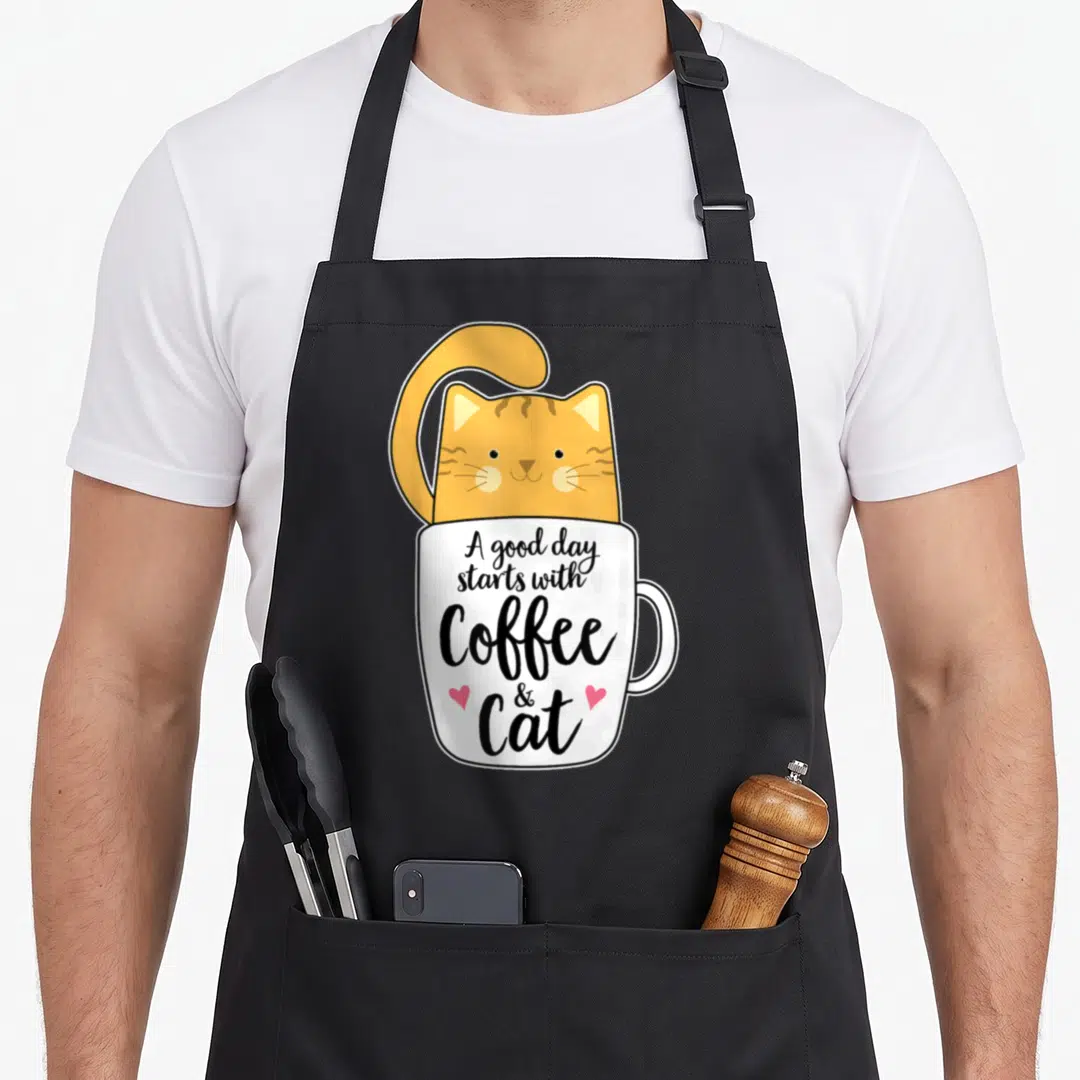 Coffee cat in an apron - Orange cat inside white coffee cup with text A good day starts with Coffee & Cat and two pink — shown on a black cotton canvas apron against a white background