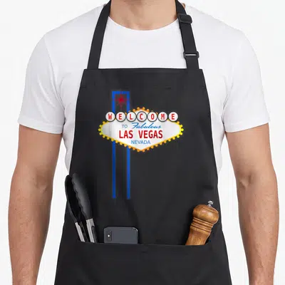 Sign las vegas apron - White diamond sign with WELCOME TO Fabulous LAS VEGAS NEVADA text, red star, blue poles, yellow — shown on a black cotton canvas apron against a white background