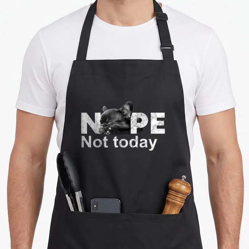 Today french bulldog apron - Sleeping french bulldog head replacing the O in NOPE Not today distressed text — shown on a black cotton canvas apron against a white background