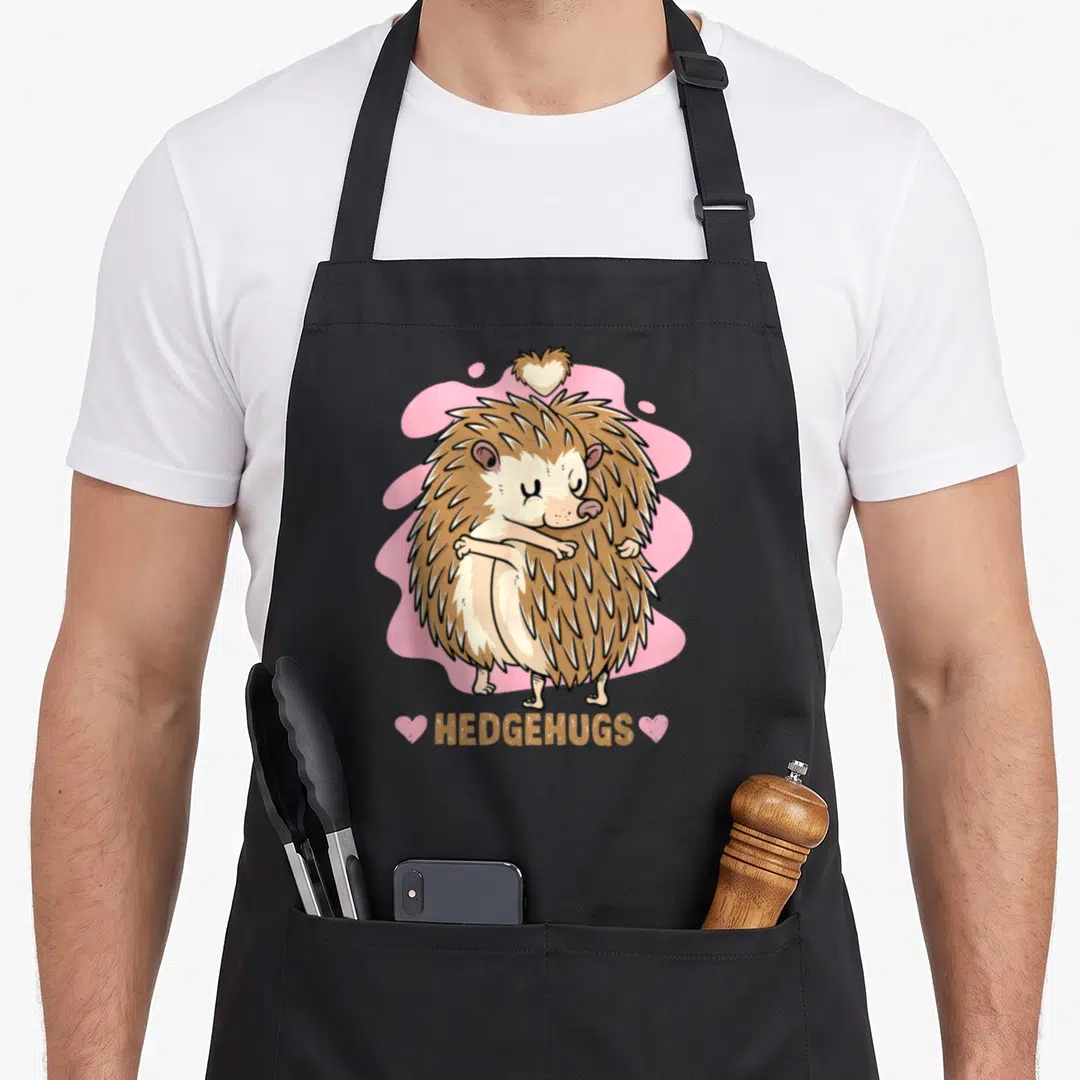 Hedgehug animal apron - Two brown hedgehogs hugging with HEDGEHUGS text and pink hearts — shown on a black cotton canvas apron against a white background