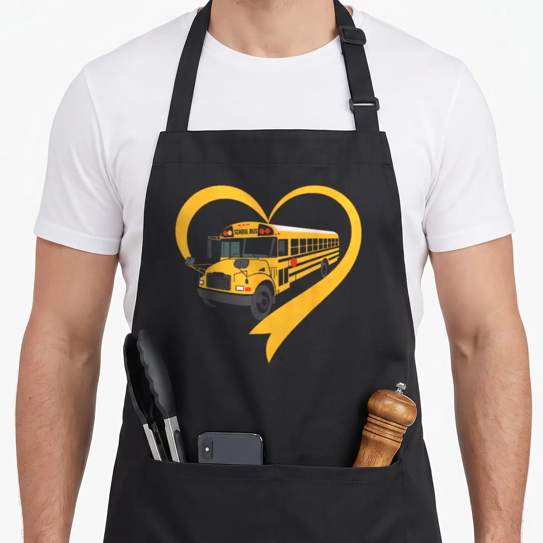 Cute driver school bus apron - Yellow school bus illustration inside a large heart outline with printed SCHOOL BUS text — shown on a black cotton canvas apron against a white background