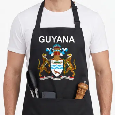 National guyana apron - Coat of Arms with two jaguars, shield, and motto One People One Nation One Destiny — shown on a black cotton canvas apron against a white background