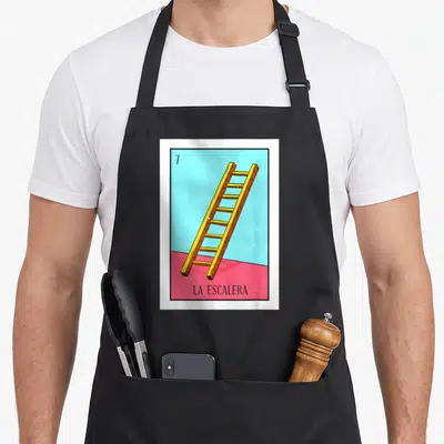 Escalera mexican apron - Yellow ladder on blue and pink background with number 7 and text LA ESCALERA — shown on a black cotton canvas apron against a white background