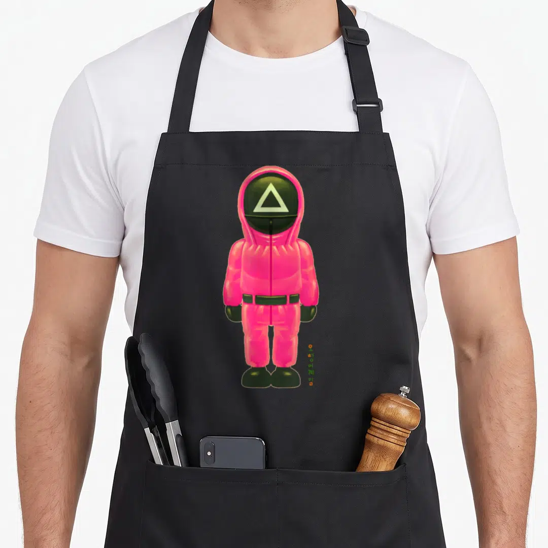 Soldier full body apron - Pink jumpsuit figure with triangle mask and vertical Korean text — shown on a black cotton canvas apron against a white background