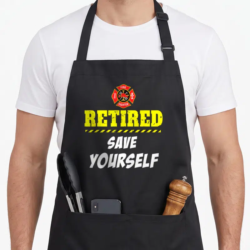 Retirement firefighter apron - Red fire emblem above yellow RETIRED text and white SAVE YOURSELF phrase — shown on a black cotton canvas apron against a white background