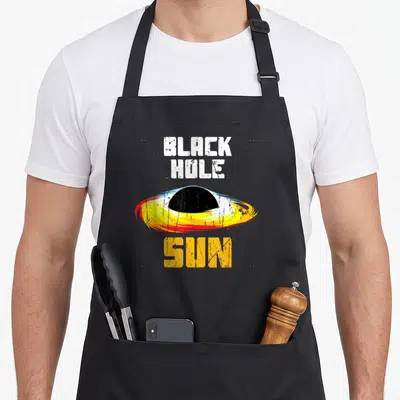 Sun black hole apron - Distressed BLACK HOLE SUN text around a black sphere with yellow red and white disk — shown on a black cotton canvas apron against a white background