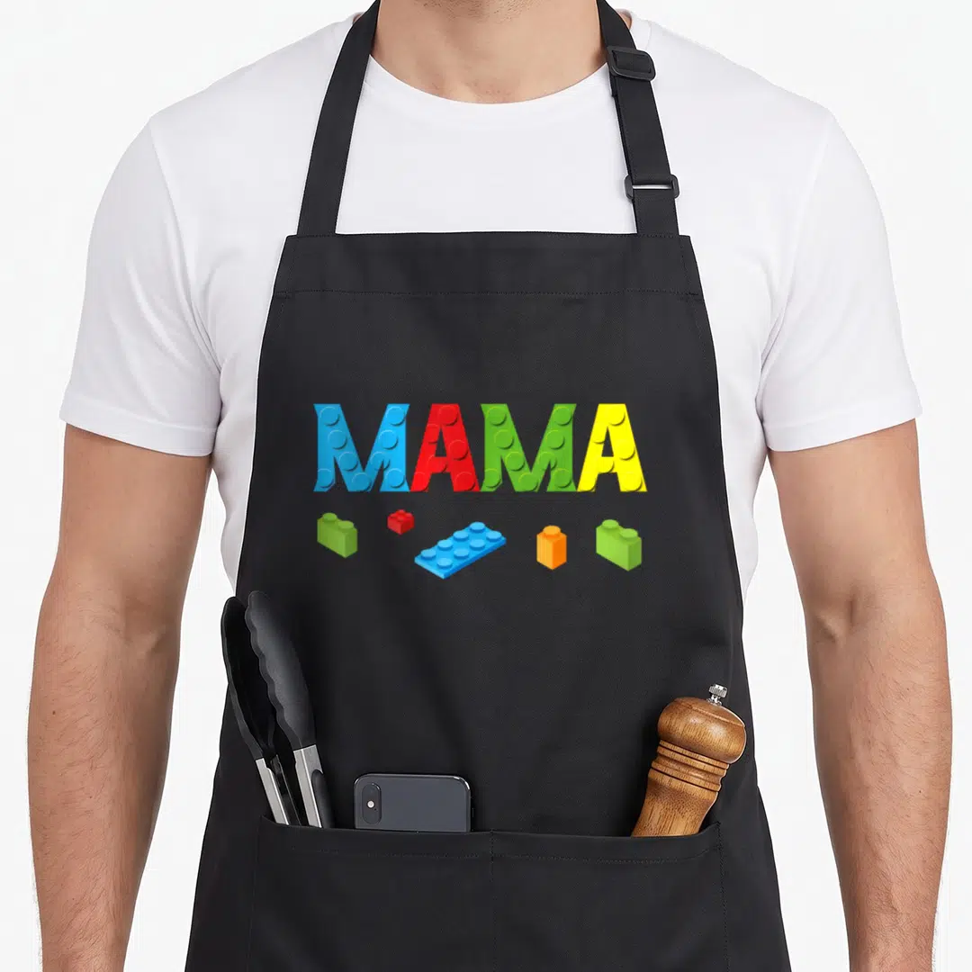 Mama building apron - MAMA text as toy bricks with five scattered blocks in blue red green yellow orange — shown on a black cotton canvas apron against a white background