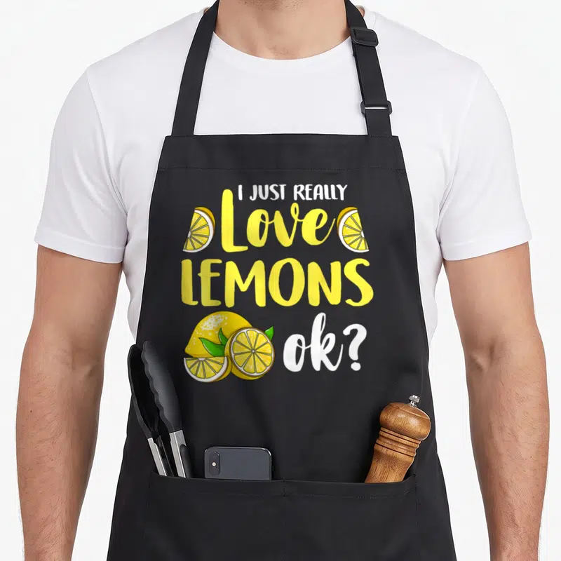 Lemon juice lemonade apron - I JUST REALLY Love LEMONS ok? text with yellow lemon slices and green leaves — shown on a black cotton canvas apron against a white background