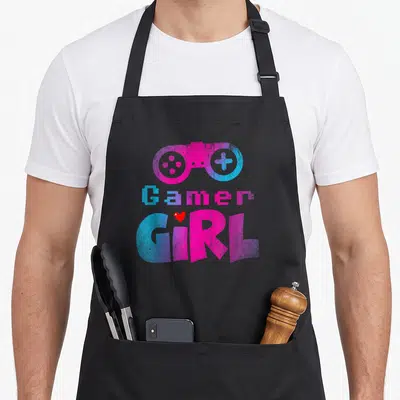 Game nerd apron - Pink blue game controller with pixel Gamer Girl text and red heart — shown on a black cotton canvas apron against a white background