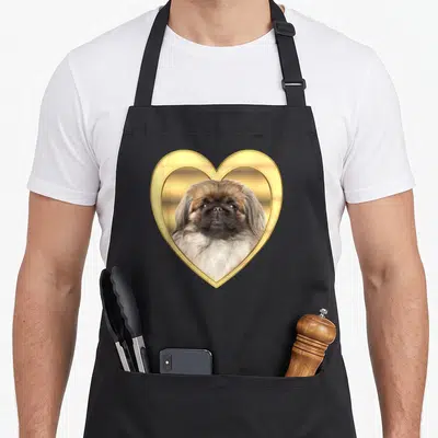 Pekingese pup apron - Dog photo inside gold heart frame with brown white fur on black apron — shown on a black cotton canvas apron against a white background