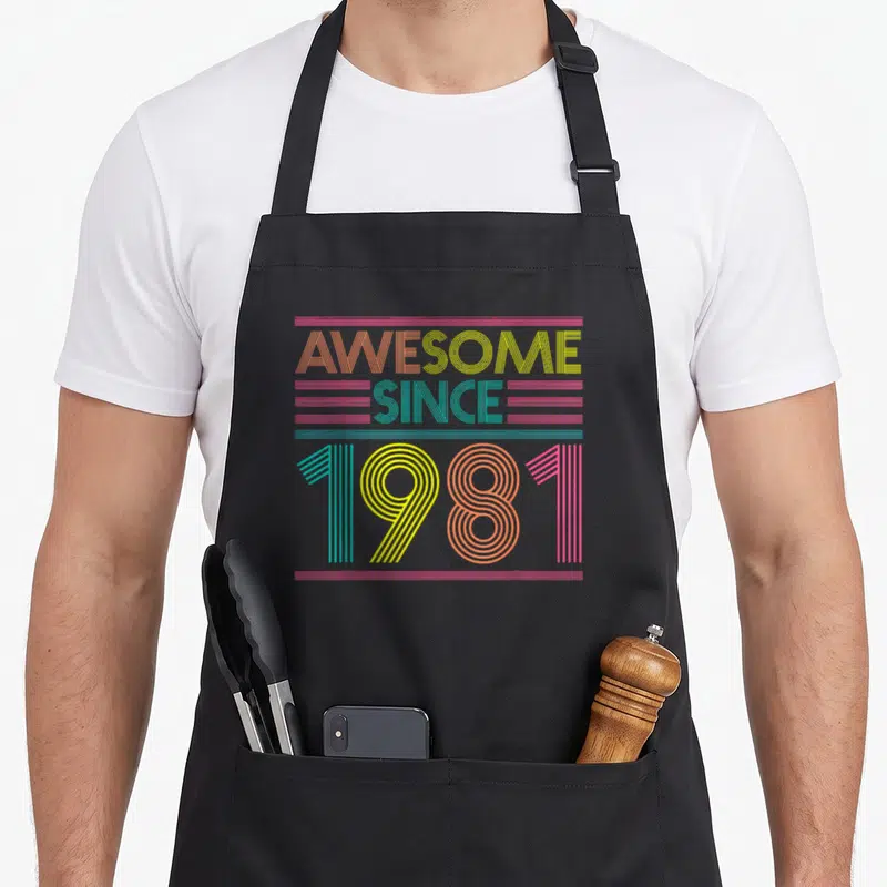 Funny 41st birthday apron - Striped text AWESOME SINCE 1981 in orange yellow teal pink lines — shown on a black cotton canvas apron against a white background