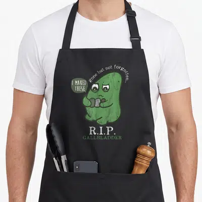 Rest anatomy apron - Cartoon green gallbladder holding stones with R.I.P. GALLBLADDER text — shown on a black cotton canvas apron against a white background