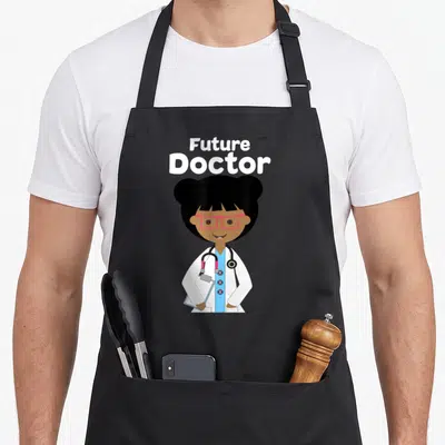 Funny future doctor apron - Cartoon girl in white lab coat and pink glasses holding clipboard under Future Doctor text — shown on a black cotton canvas apron against a white background