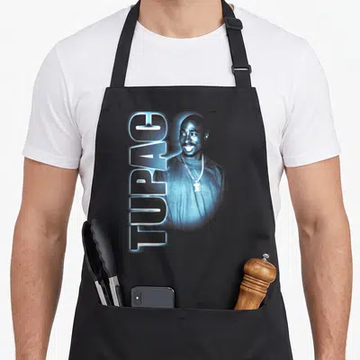 Glowing tupac apron - Blue tinted Tupac photo with vertical TUPAC text running down the left side — shown on a black cotton canvas apron against a white background