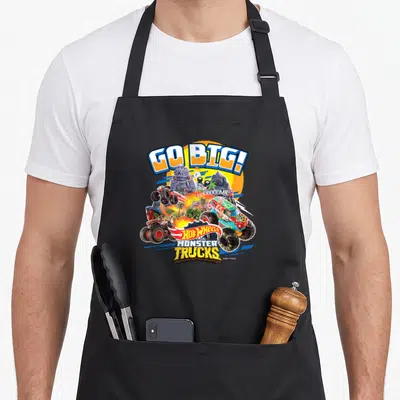 Hobby truck aprons - GO BIG! text over monster trucks, palm trees, and Hot Wheels logo in yellow blue red green — shown on a black cotton canvas apron against a white background