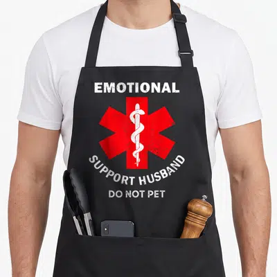 Emotional support pet husband apron - Red Star of Life with white Rod of Asclepius and distressed white text on black — shown on a black cotton canvas apron against a white background