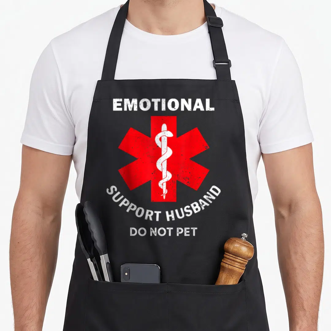 Emotional support pet husband apron - Red Star of Life with white Rod of Asclepius and distressed white text on black — shown on a black cotton canvas apron against a white background