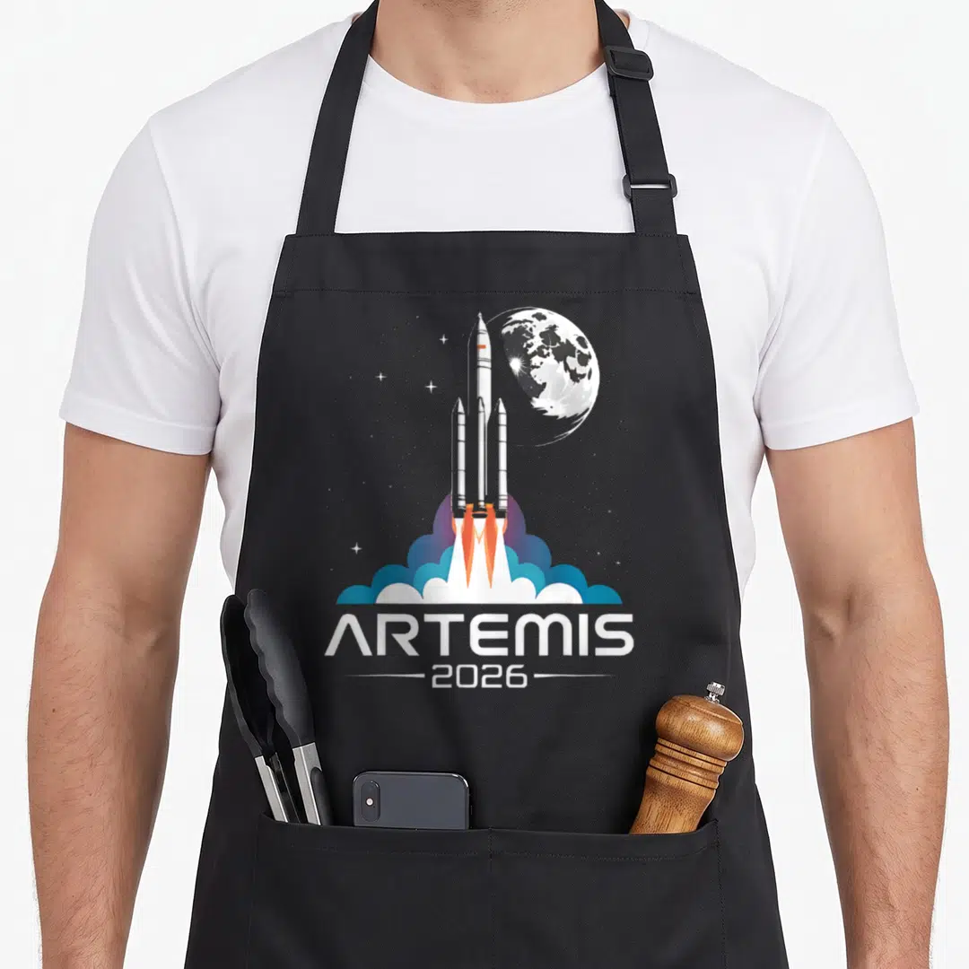 Artemis moon apron - Minimalist rocket launch with ARTEMIS 2026 text, moon, and stars in white blue orange grey — shown on a black cotton canvas apron against a white background